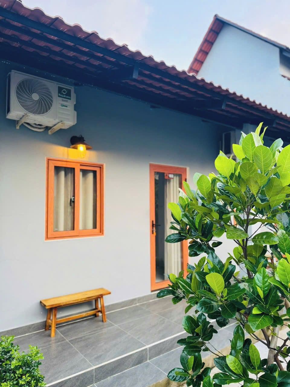 Uma casa com varanda de telhado, um banco e um vaso com planta.