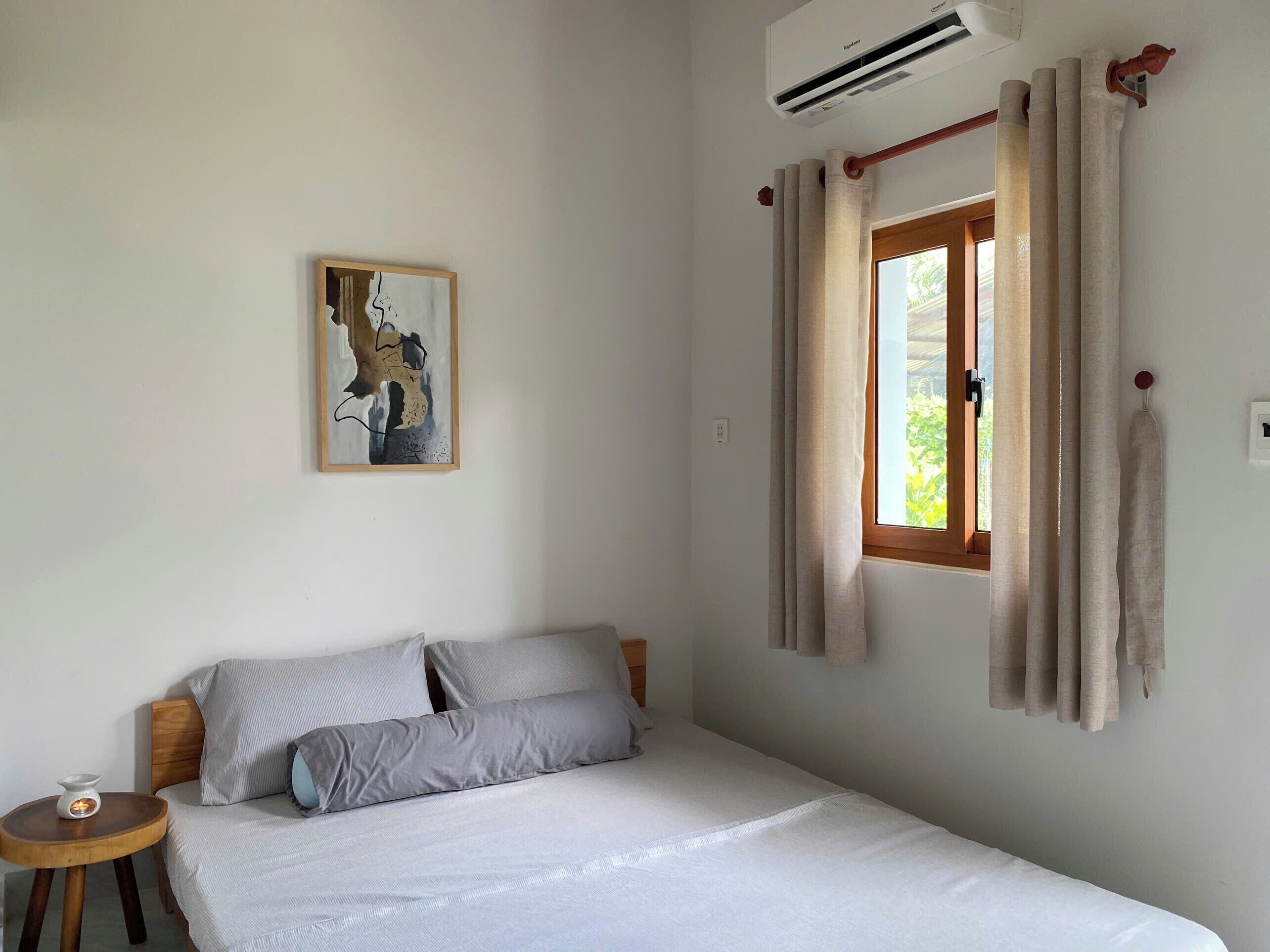 Um quarto com cama, mesa de cabeceira, ar condicionado na parede e janela com cortinas.