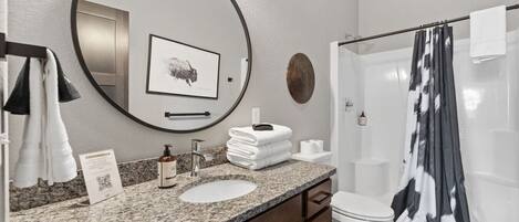 A bathroom with a round mirror, a sink, a toilet, and a shower with a black and white curtain.