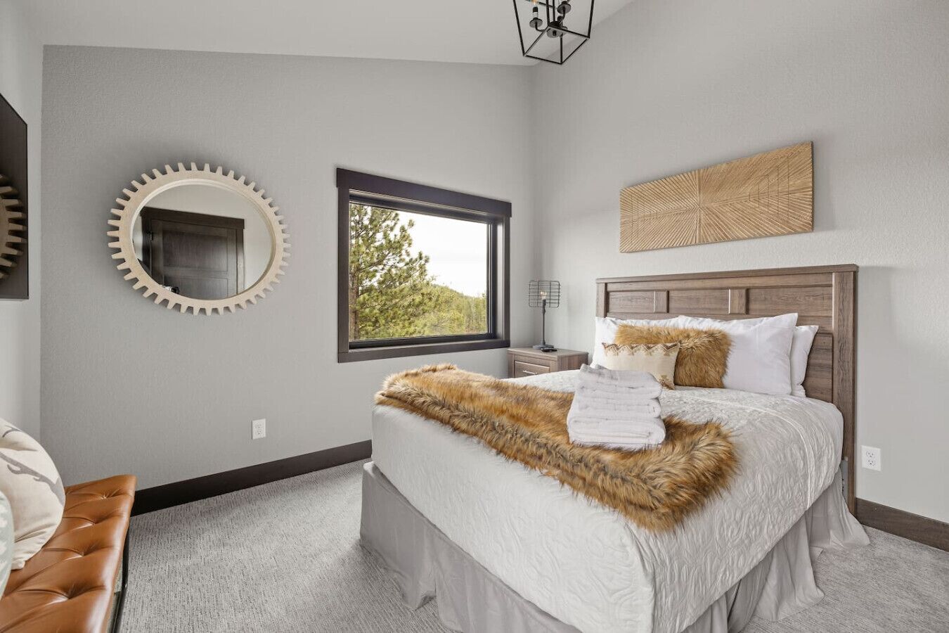 A bedroom with a large bed, a round mirror, a window with a view of trees, and a wooden headboard.