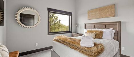 A bedroom with a large bed, a round mirror, a window with a view of trees, and a wooden headboard.
