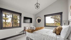A bedroom with a large bed, two windows, a TV, and a mirror. - MK Hideaway Mountain Cabin w/ Hot Tub (Lead)