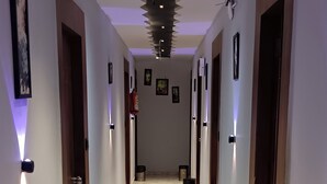 Un pasillo con suelo de mármol, puertas de madera y lámparas fijadas a la pared.