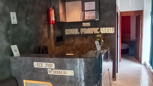 Zona de recepción de un hotel con suelo de mármol, mostrador de recepción, ventilador de techo y extintor.