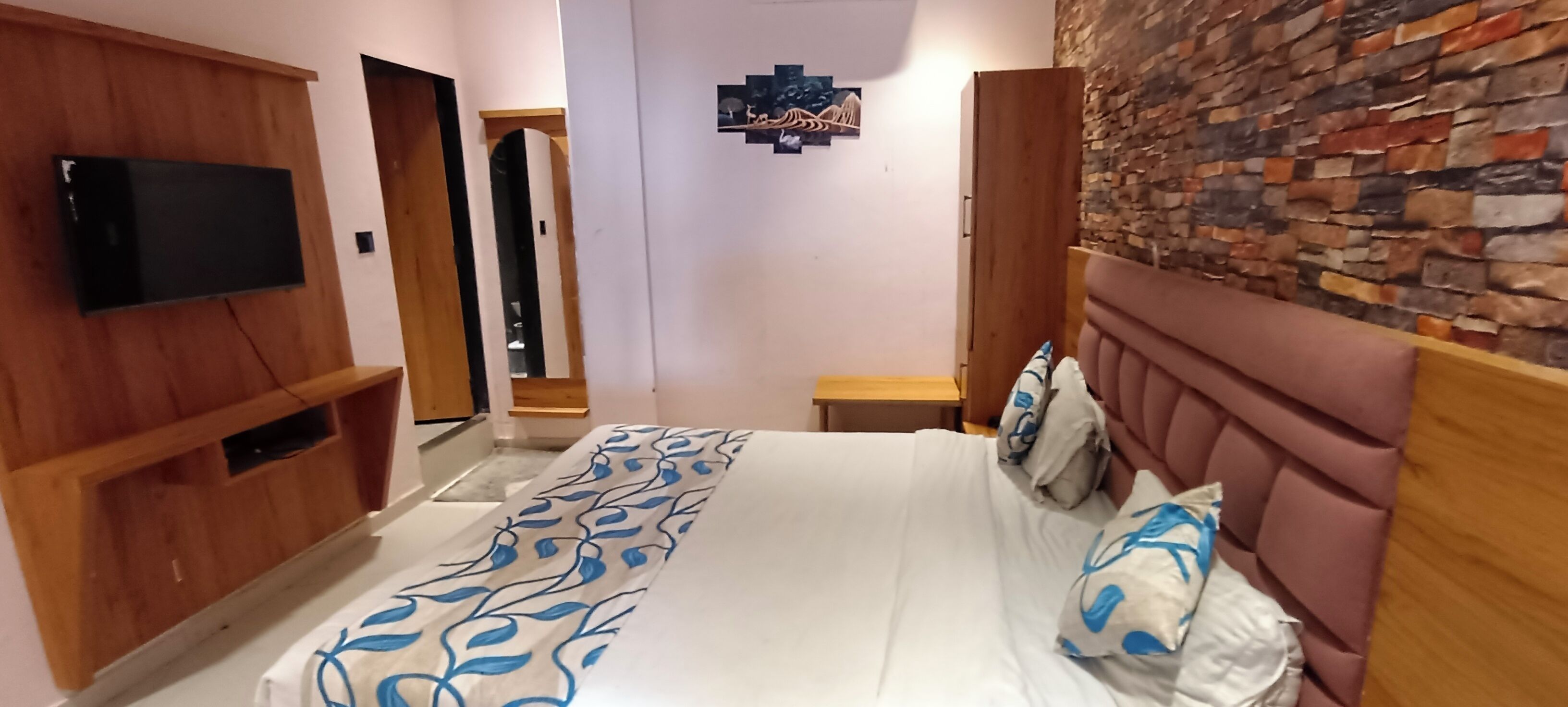 A bedroom with a bed, a television, a wooden wardrobe, a stone wall, and a door leading to another room.