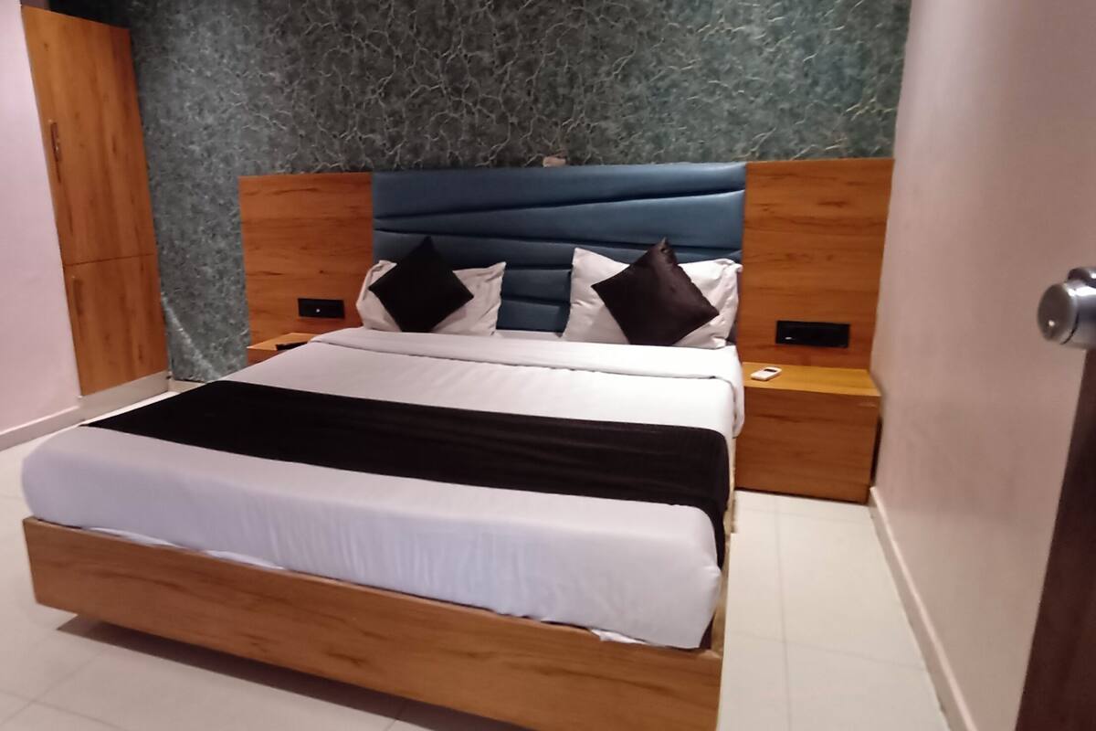 A modern bedroom with a wooden bed, a blue upholstered headboard, and a marble-patterned wall.