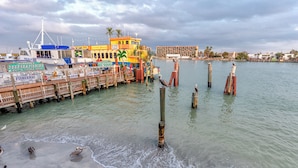 Ein Ufergebiet mit vor Anker liegenden Booten, Holzpfählen im Wasser und einem Gebäude mit Schild für einen Angelbedarfsladen.
