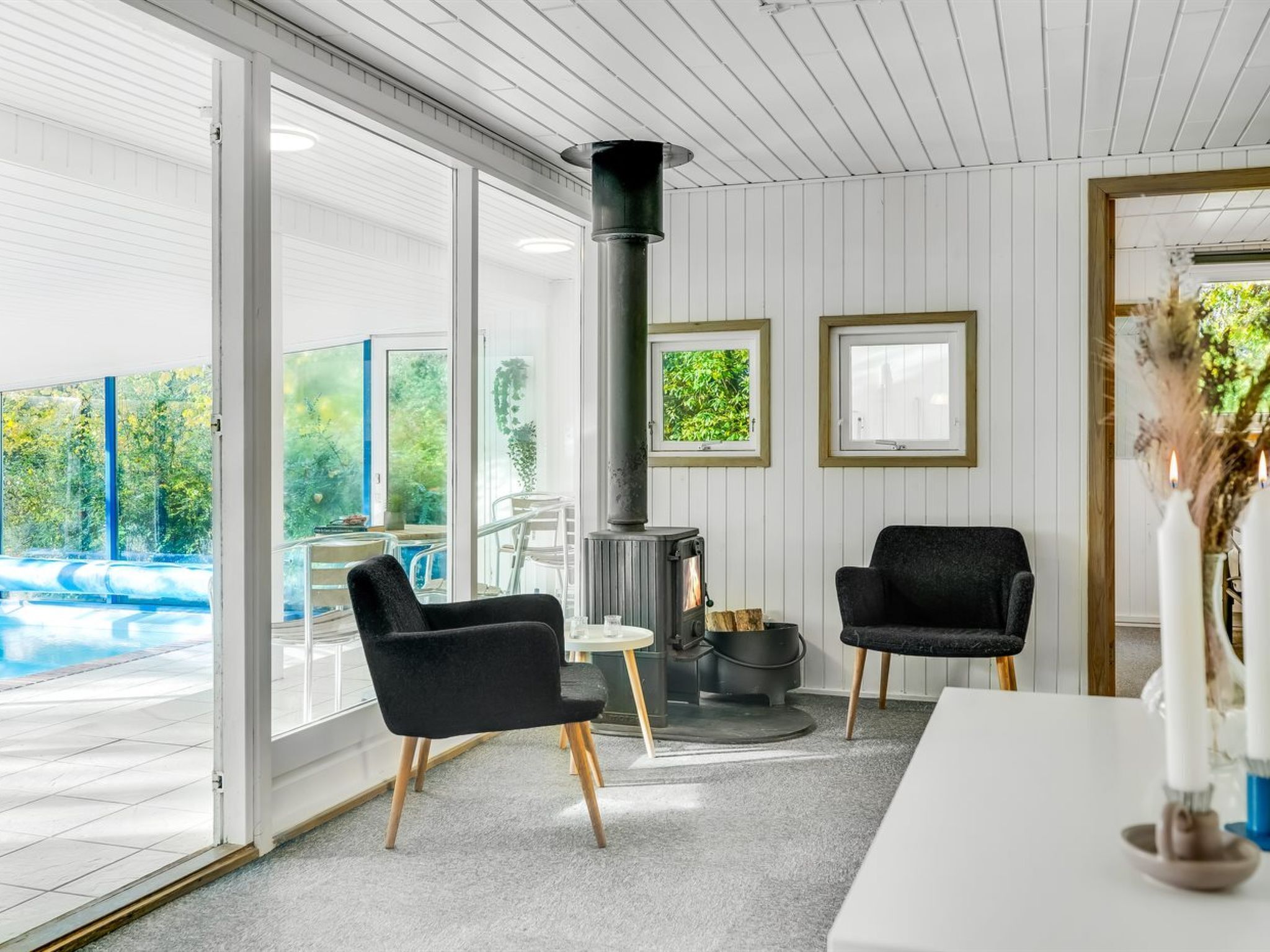 Un intérieur moderne avec une cheminée, deux chaises noires, une table à manger et une vue sur une piscine.