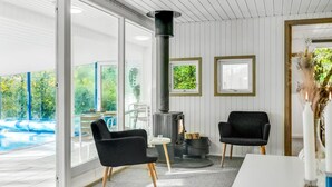 A modern interior with a fireplace, two black chairs, a dining table, and a view of a swimming pool.