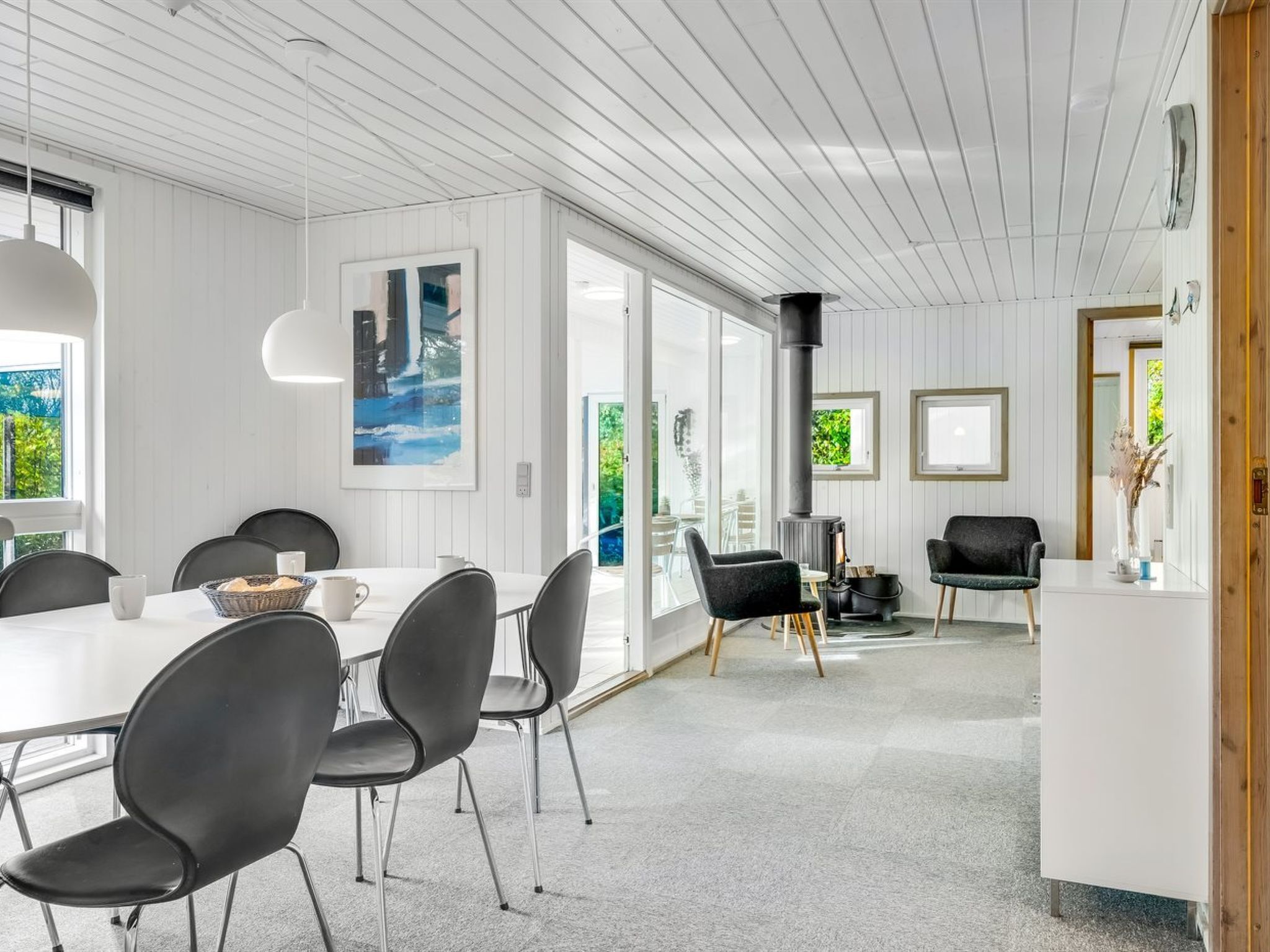 Un espace repas moderne avec une table blanche et des chaises noires, une grande fenêtre et une vue sur la verdure à l’extérieur.