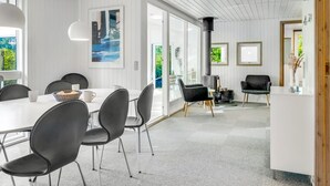 A modern dining area with a white table and black chairs, a large window, and a view of greenery outside.