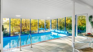 An indoor swimming pool with clear glass walls, a tiled floor, and a bench.
