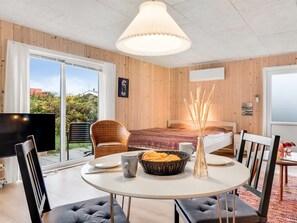 Ein gemütliches Zimmer mit einem Bett, einem Esstisch mit Stühlen, einem Fernseher und einem großen Fenster mit Blick auf Grünflächen.