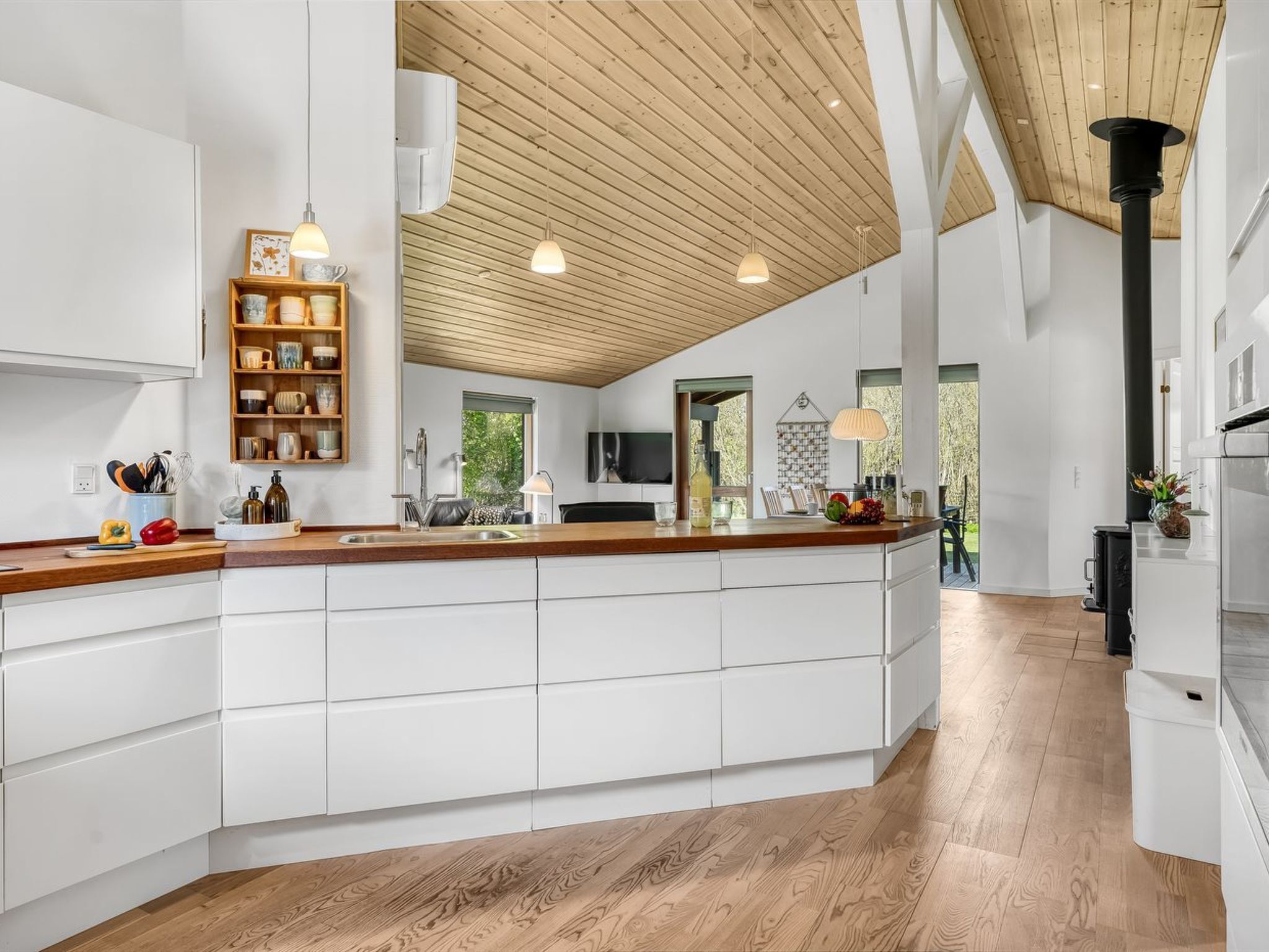 A modern kitchen with white cabinetry, a wooden ceiling, and pendant lighting.