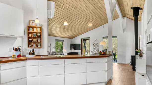Une cuisine moderne avec des meubles blancs, un plafond en bois et des luminaires suspendus.
