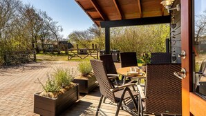 Un espace extérieur aménagé, abrité et doté de chaises en osier et d’une table, entouré de jardinières et d’une terrasse en bois.