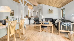 Un vaste espace de vie doté d’un plafond en bois, d’une table à manger avec des chaises, d’un canapé et d’une table basse.