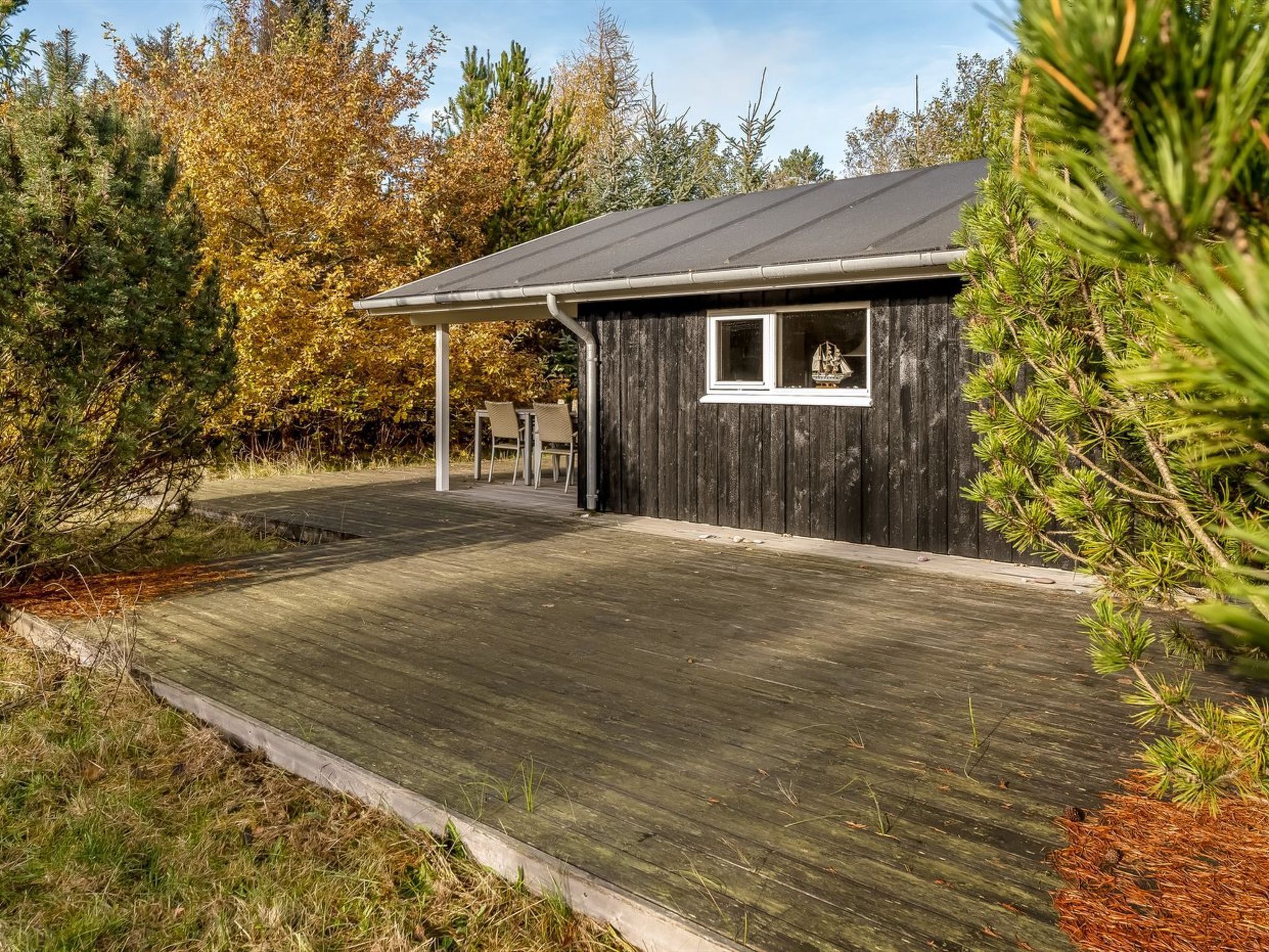 A wooden cabin with a metal roof, a small window, and a covered outdoor seating area.
