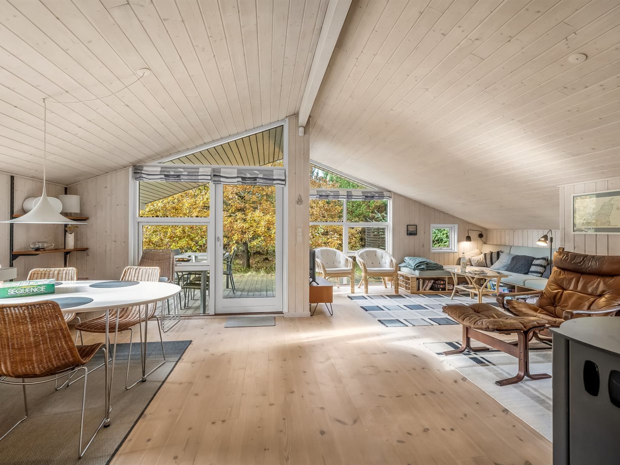 A spacious loft with a high ceiling, open-plan living and dining areas, large windows, and a view of trees.
