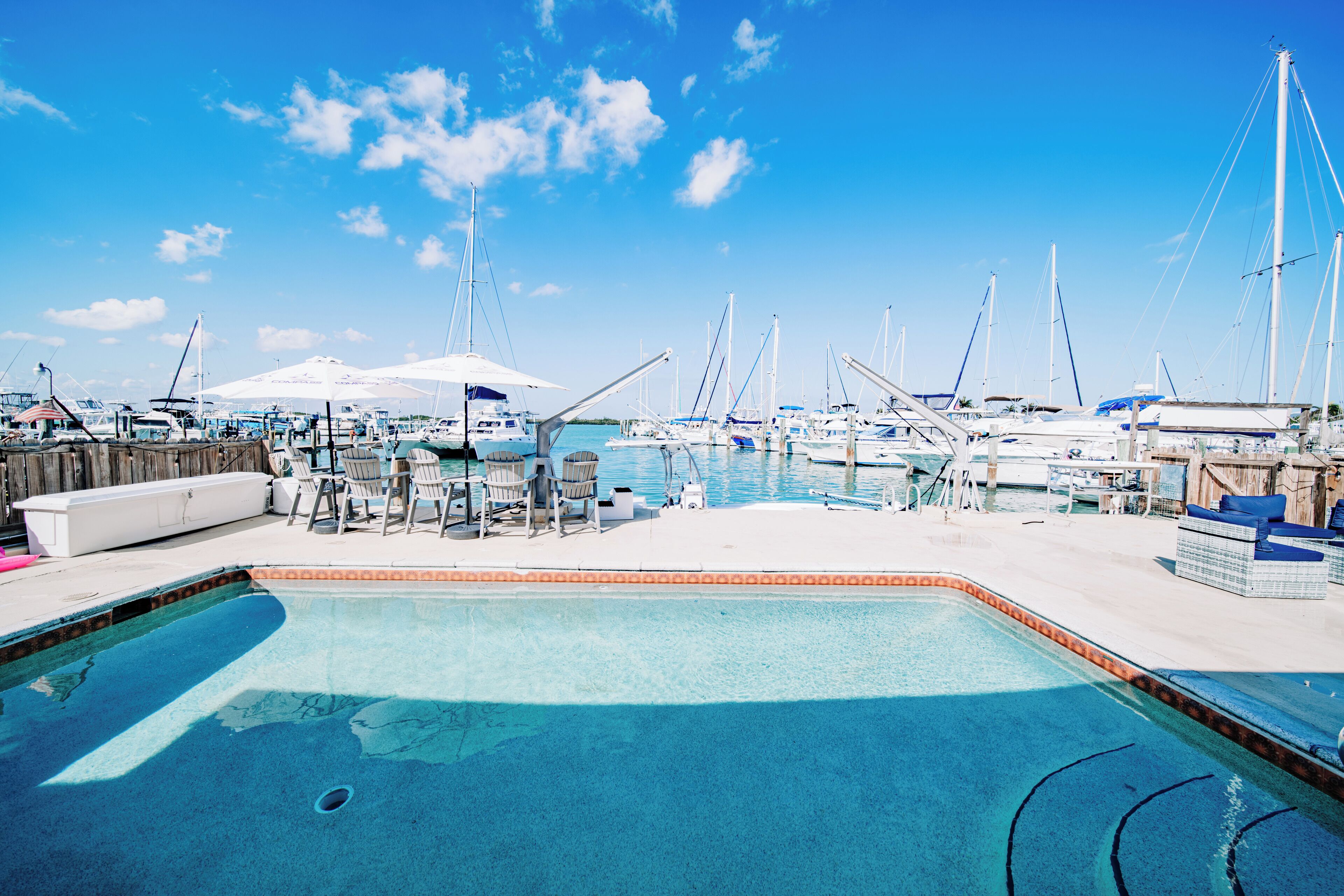 A marina with boats docked, a swimming pool, and lounge chairs.