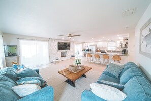 A spacious living room with a large sofa set, a coffee table, and a kitchen area in the background. - Waterfront Pool House on Hutchinson Island (Fort Pierce)
