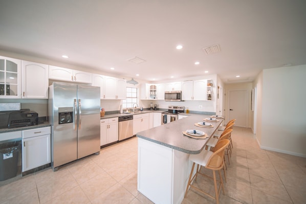 A modern kitchen with white cabinets, stainless steel appliances, and a central island with bar stools. - Waterfront Pool House on Hutchinson Island (Fort Pierce)