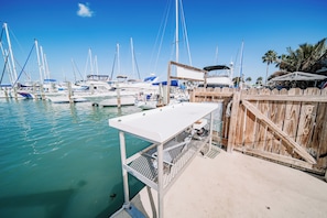 A marina with multiple boats docked, a wooden fence, and a white table with metal mesh. - Waterfront Pool House on Hutchinson Island (Fort Pierce)
