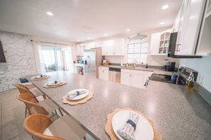 A modern kitchen with a large island, white cabinets, and a stone accent wall. - Waterfront Pool House on Hutchinson Island (Fort Pierce)