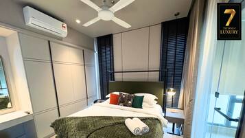 A modern hotel room with a bed, a ceiling fan, a window with blinds, a bedside table, and a view of the outside.