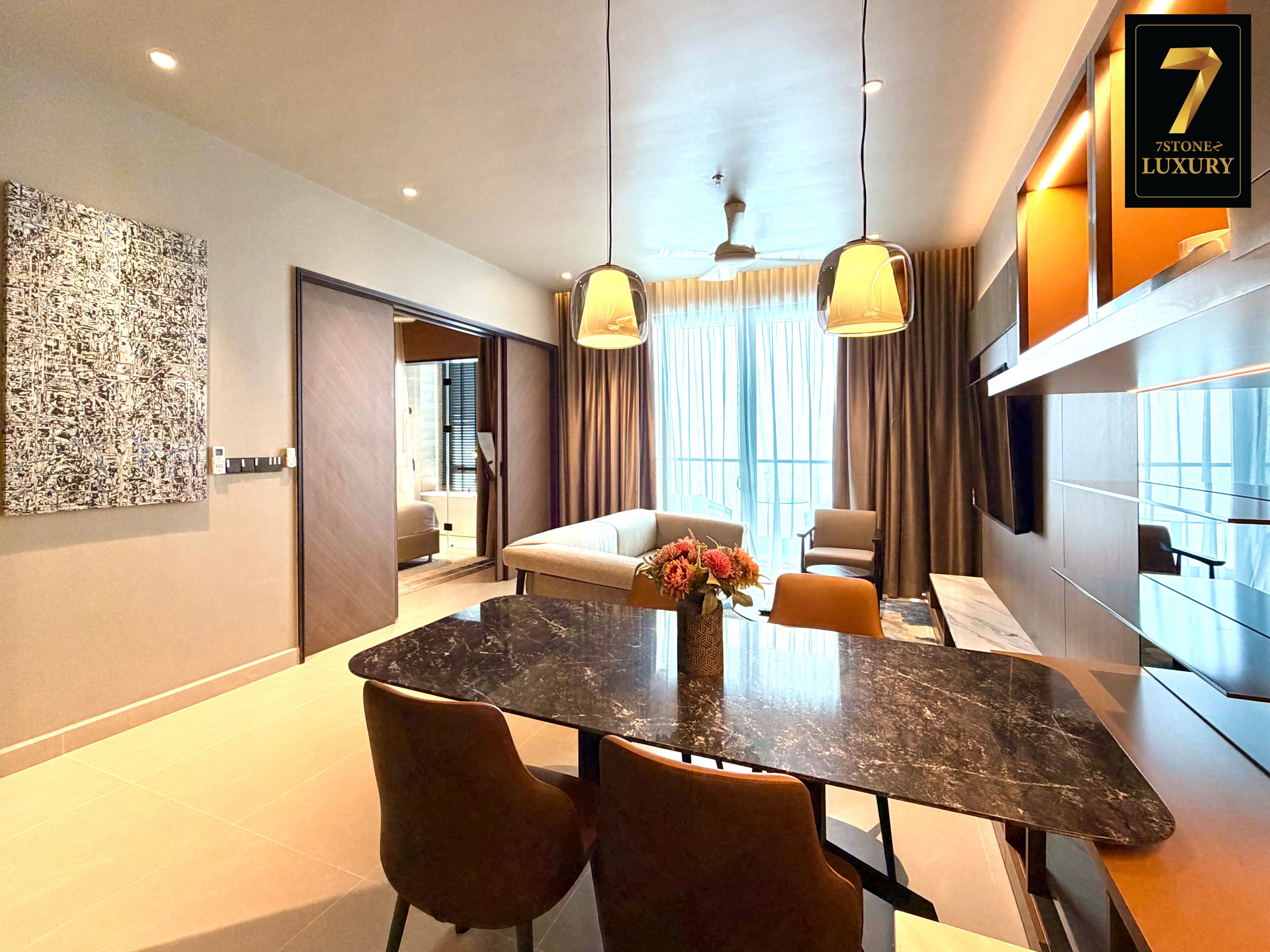 A modern hotel room with a dining area, a sofa, and a TV mounted on the wall.
