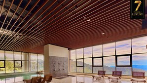 Un hall d’entrée spacieux avec un plafond haut, de grandes fenêtres donnant sur les montagnes et plusieurs bancs en bois.