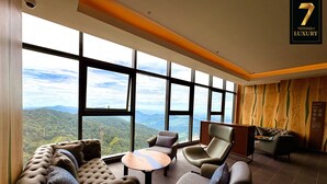 Une pièce spacieuse avec de grandes fenêtres donnant sur les montagnes, un canapé moelleux, une table basse ronde et un fauteuil en cuir.