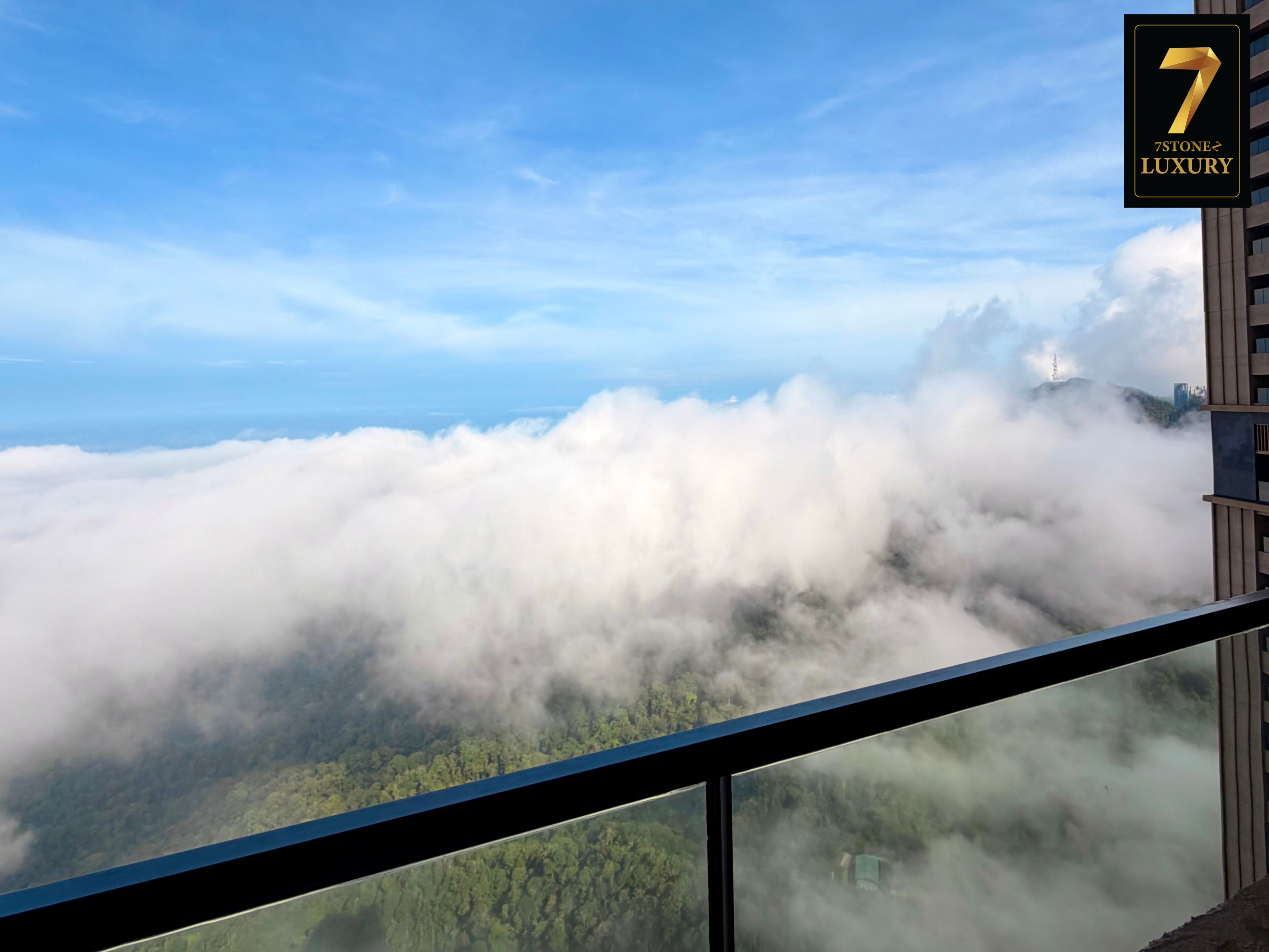 A high-rise hotel with a view of a forested landscape and clouds below.