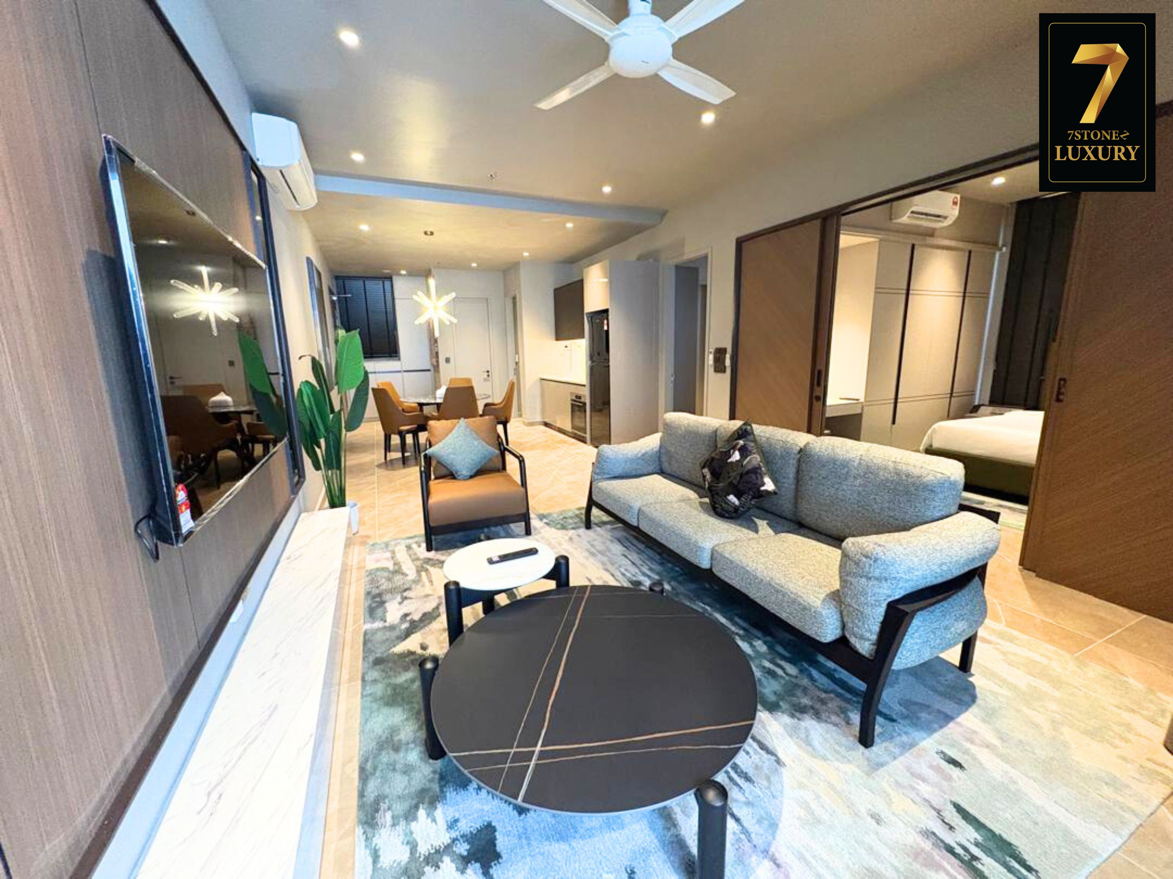 A modern living room with a sofa, coffee table, and chairs, a large mirror, and a ceiling fan.