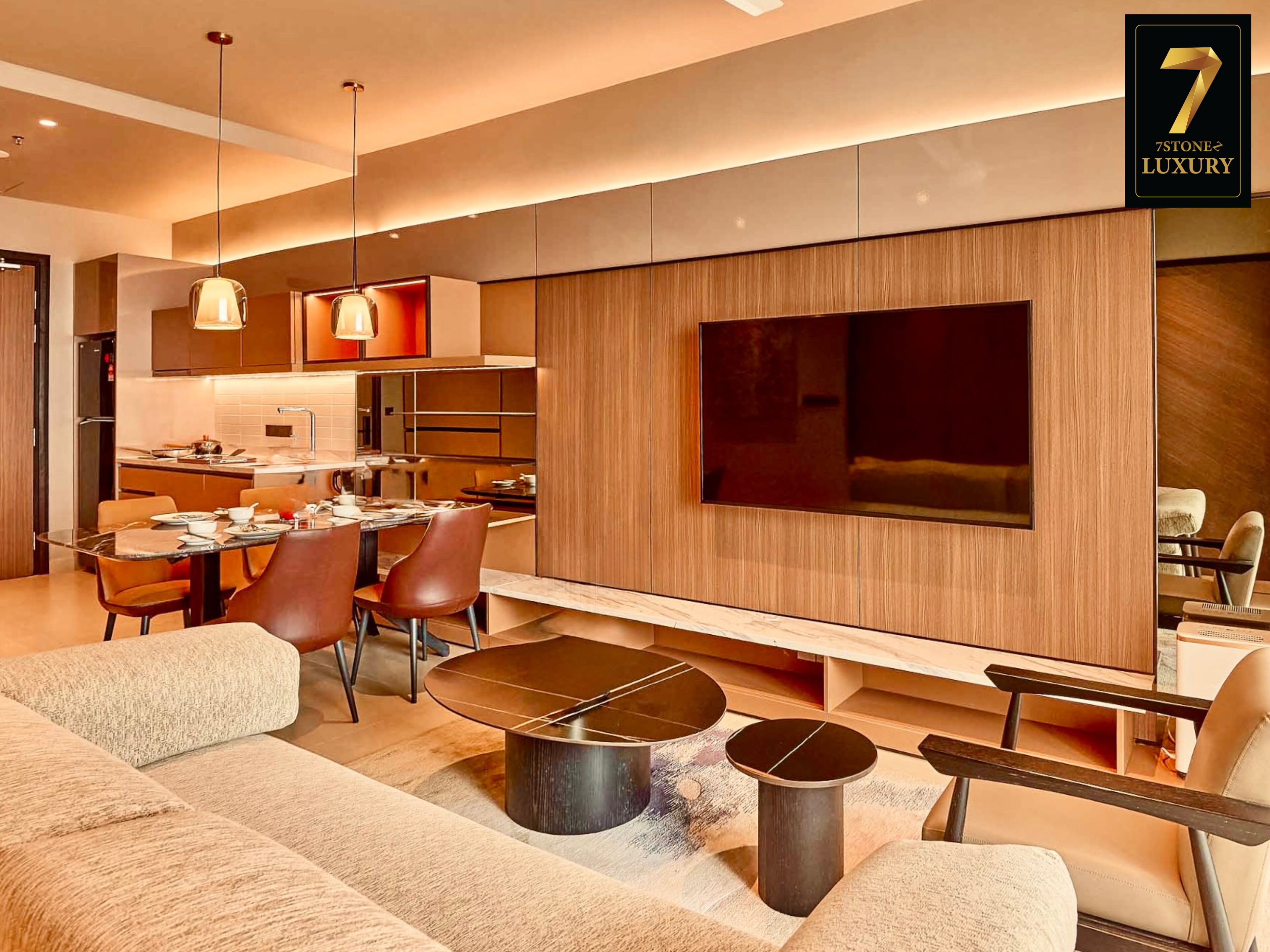 A modern living room with a sofa, coffee table, and TV. There is a dining area with chairs and a table. The room has wooden paneling and a large window.