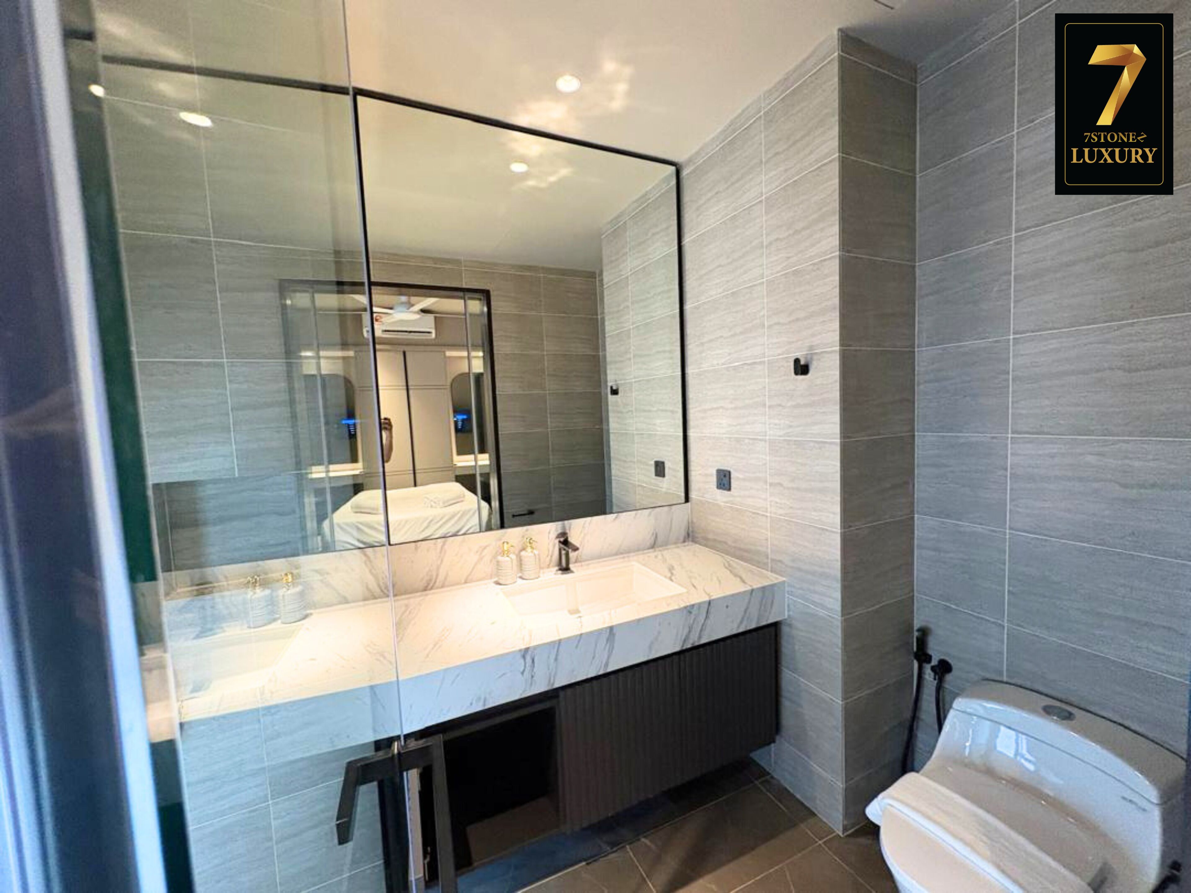 A modern bathroom with a large mirror, a marble countertop, and a toilet.