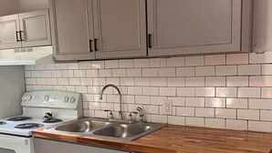 Une cuisine avec des meubles blancs, un plan de travail en bois, un évier en acier inoxydable et une cuisinière blanche.