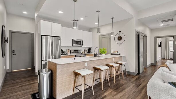 Una cocina moderna con una isla central, electrodomésticos de acero inoxidable y taburetes de bar.