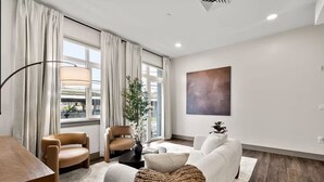 Una sala de estar moderna con un sofá, dos sillones, una mesa de centro y un ventanal con cortinas.
