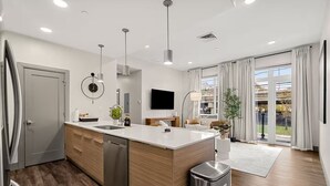 Una cocina moderna con una isla central, lavavajillas integrado y un amplio ventanal con cortinas.