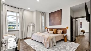 Habitación de hotel moderna con una cama grande, una mesita de noche, un televisor de pantalla plana y vistas a la ciudad desde la ventana.