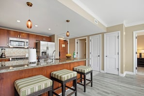 Una cocina con armarios de madera, un refrigerador de acero inoxidable, un microondas, un fregadero y dos taburetes de bar.