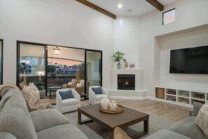 Een moderne woonkamer met een open haard, een flatscreen televisie en een uitzicht door grote glazen deuren.
