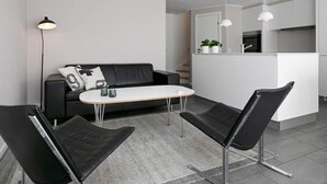 Ein modernes Wohnzimmer mit einer schwarzen Ledersofa, einem weißen Couchtisch und schwarzen Stühlen. Es gibt eine Küchenzeile mit weißen Schränken und einer Arbeitsplatte.