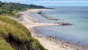 En kustnära strand med steniga stränder, klar himmel och träd i fjärran.