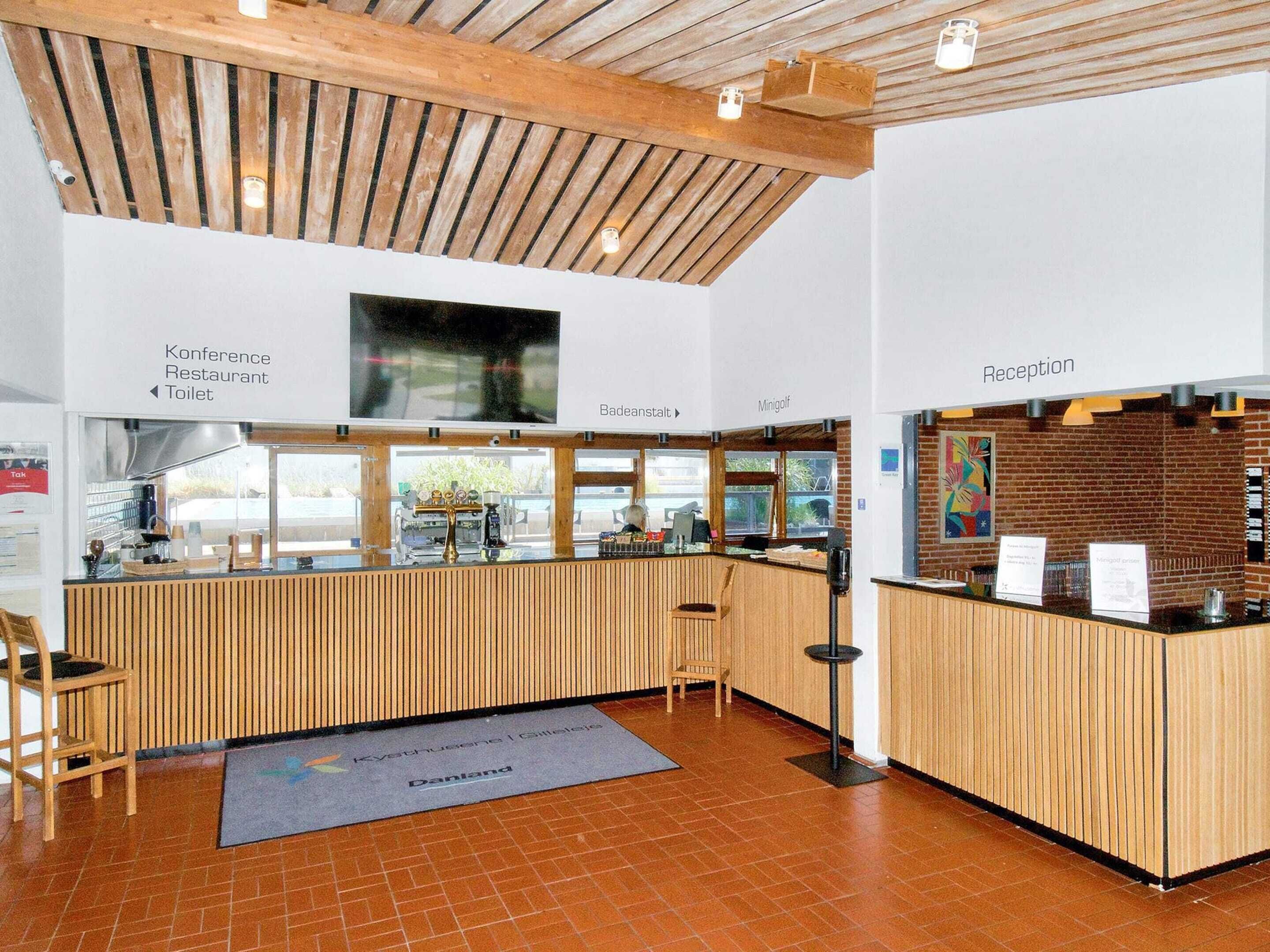 Un espace d’accueil comprenant un comptoir en bois, un bureau d’accueil et des panneaux indicateurs pour la salle de conférence, le restaurant et les toilettes.