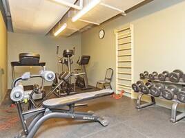 A gym with exercise equipment, a bench, dumbbells, and a clock on the wall.