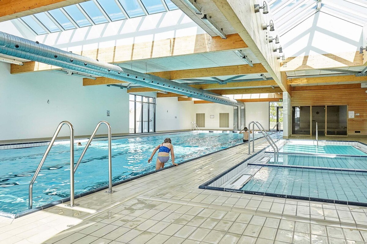 Une piscine intérieure à l’eau claire, dotée d’échelles en métal et d’un sol carrelé.