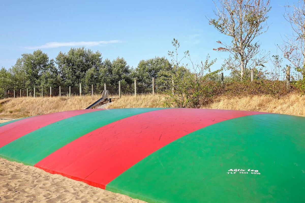 Una estructura inflable grande y colorida en una playa arenosa, con una cerca y árboles al fondo.