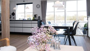 A modern kitchen with a dining area, large windows, and a flower arrangement on the table.